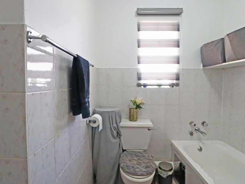 A functional bathroom featuring a bathtub, toilet, and neutral wall tiling, complemented by a window with a fitted blind.