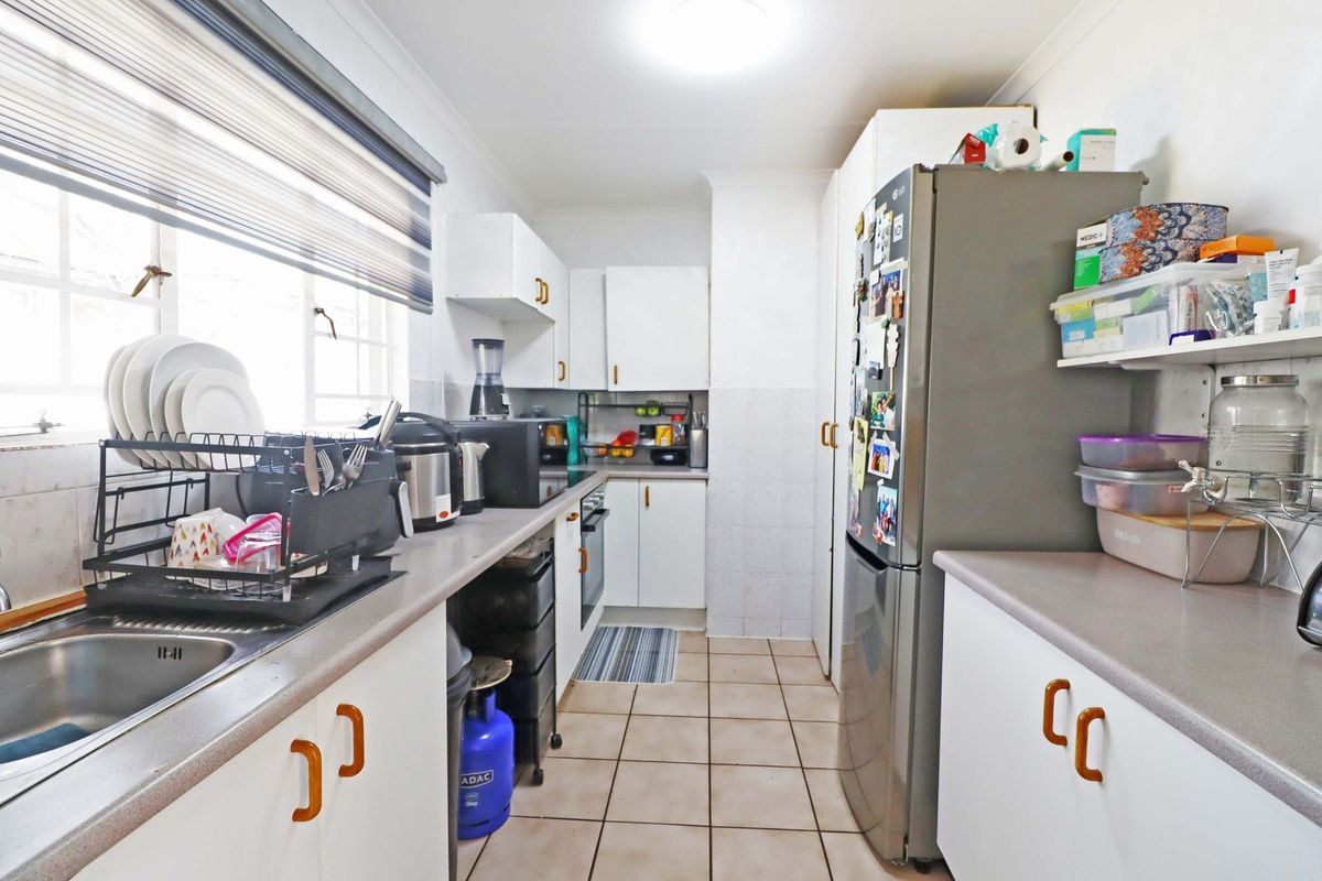 A functional galley-style kitchen featuring white cabinetry, laminate countertops, tiled flooring, and a built-in oven, offering a practical layout for daily meal preparation.