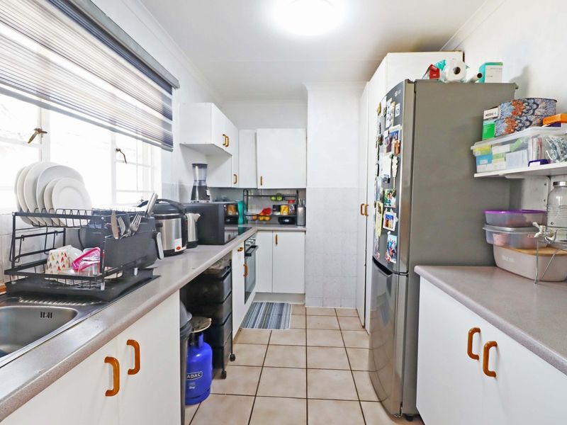 A functional galley-style kitchen featuring white cabinetry, laminate countertops, tiled flooring, and a built-in oven, offering a practical layout for daily meal preparation.
