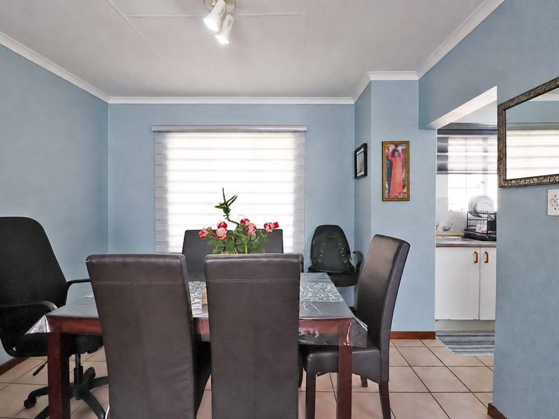 A dining area featuring tiled flooring, cove cornicing, and a window with roller blinds, with an adjacent view into the kitchen area.
