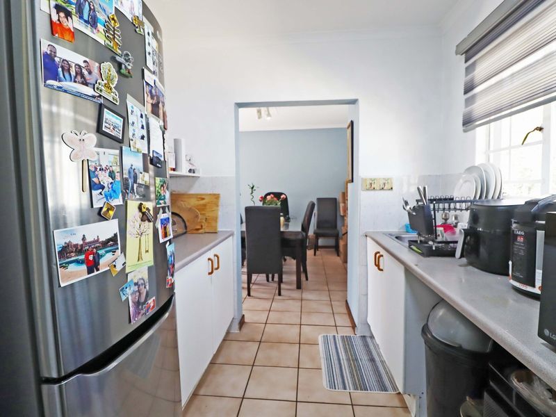 A functional galley-style kitchen featuring tiled flooring, laminate countertops, and built-in cabinetry, with a direct view into the adjacent dining area.