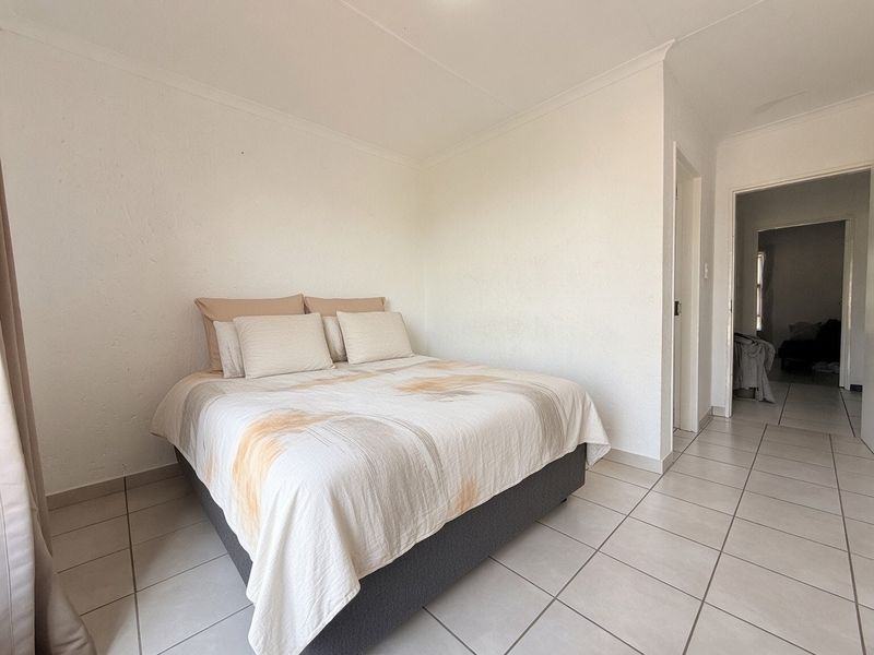 A simple bedroom featuring neutral tiled flooring and white walls, providing a clean and functional space with direct access to an adjacent hallway.