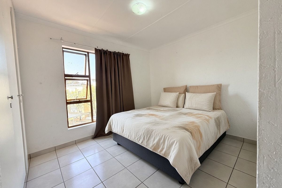 A simple bedroom featuring tiled flooring, a built-in cupboard, and a window providing natural light.