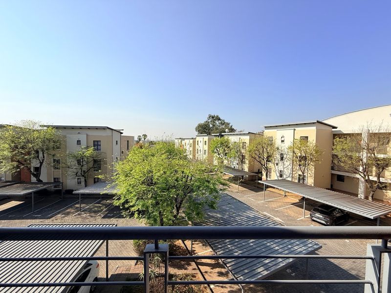 Elevated balcony view overlooking the apartment complex parking area with covered carports and landscaped trees.