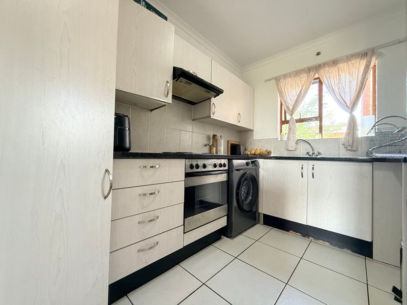 A functional kitchen featuring light-toned cabinetry, tiled flooring, a built-in oven with extractor fan, and a stainless steel sink under a window.
