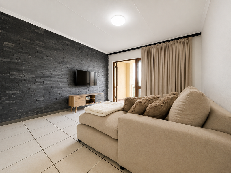 A well-maintained living room featuring a striking dark stacked stone feature wall, neutral tiled flooring, and direct access to an outdoor balcony.