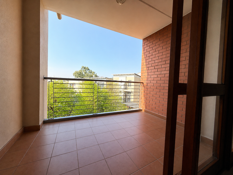 A clean, covered balcony featuring tiled flooring, an exposed brick feature wall, and a modern metal balustrade overlooking the surrounding neighborhood.