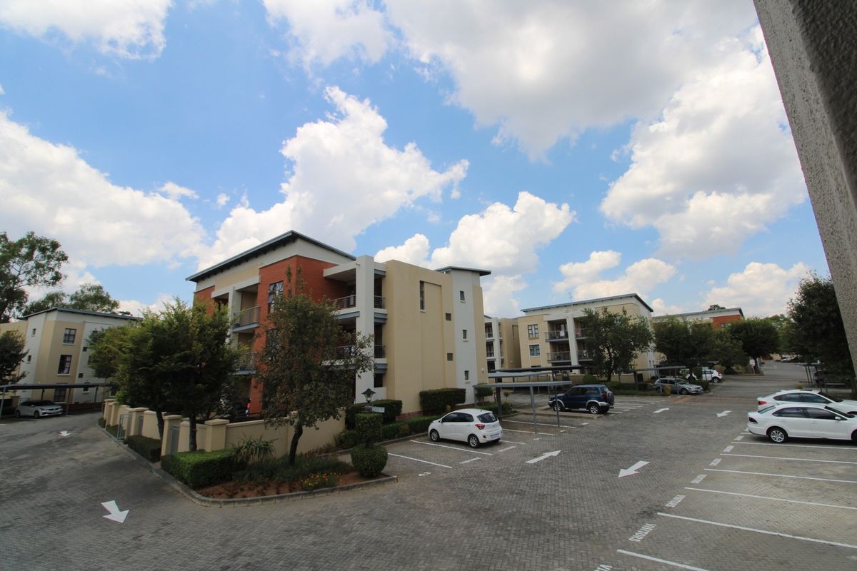 An elevated view of the apartment complex exterior, featuring paved parking bays, covered parking structures, and landscaped garden areas.