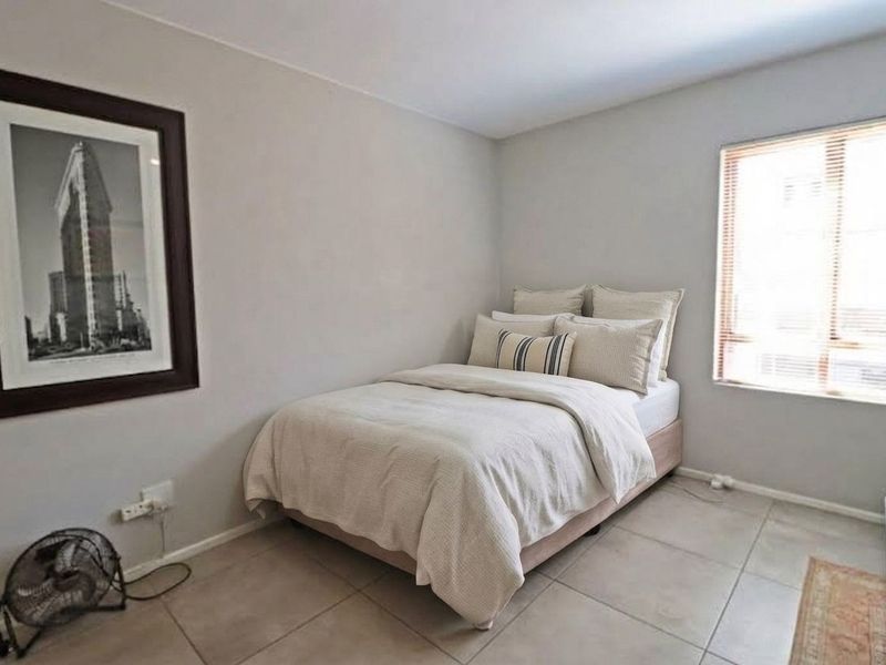 A functional bedroom featuring neutral wall tones, tiled flooring, and a window fitted with blinds, providing a clean and simple living space.