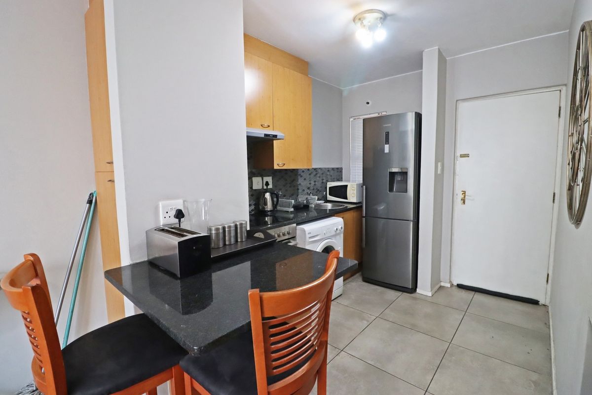 Compact open-plan kitchen featuring granite countertops, built-in cabinetry, and tiled flooring, seamlessly integrated with a small dining area.