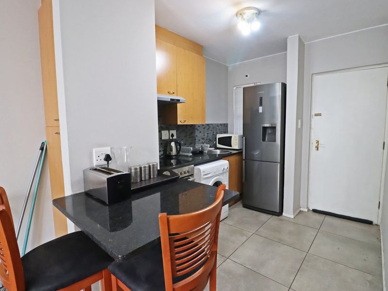 Compact open-plan kitchen featuring granite countertops, built-in cabinetry, and tiled flooring, seamlessly integrated with a small dining area.