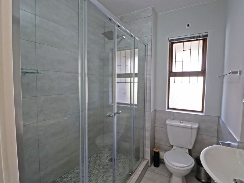 Modern bathroom featuring a glass-enclosed shower with a rain shower head, mosaic tile flooring, pedestal basin, and neutral ceramic wall tiles.