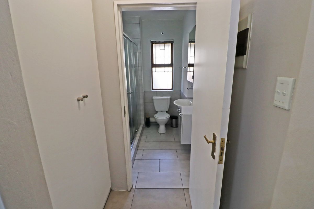 A functional bathroom featuring a shower enclosure, pedestal basin, and toilet with neutral tiled flooring and natural light from a window.