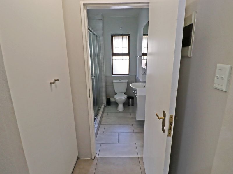 A functional bathroom featuring a shower enclosure, pedestal basin, and toilet with neutral tiled flooring and natural light from a window.