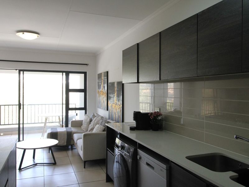 Modern open-plan apartment featuring a sleek kitchen with dark cabinetry, tiled flooring, and seamless access to a private balcony.