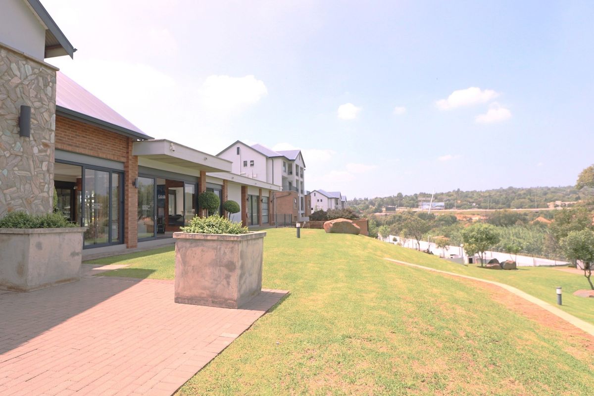 A well-maintained rear exterior view of the apartment complex featuring brick paving, stone-clad walls, large sliding glass doors, and a spacious landscaped lawn.