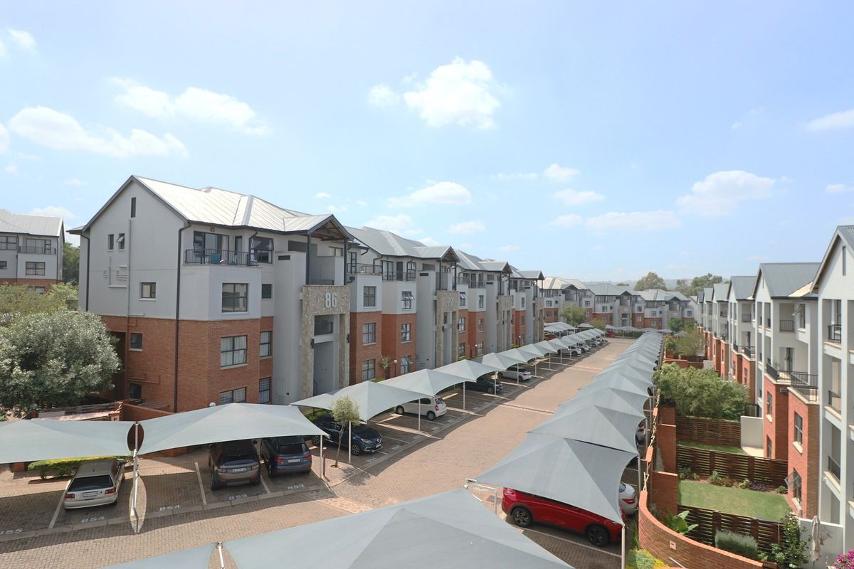 An elevated view of a modern apartment complex featuring brick and render facades, paved driveways, and extensive covered parking bays.