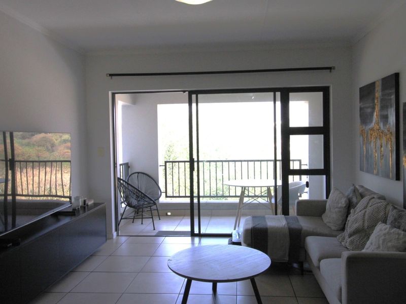A living room featuring tiled flooring and a large sliding glass door that provides direct access to an outdoor balcony area.