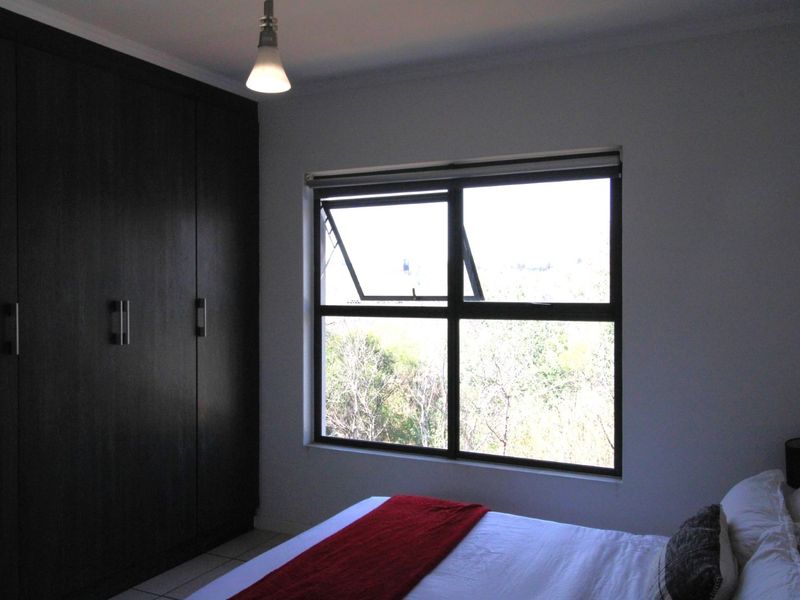 A bedroom featuring dark wood built-in cupboards and an aluminium window frame with a view of the surrounding greenery.