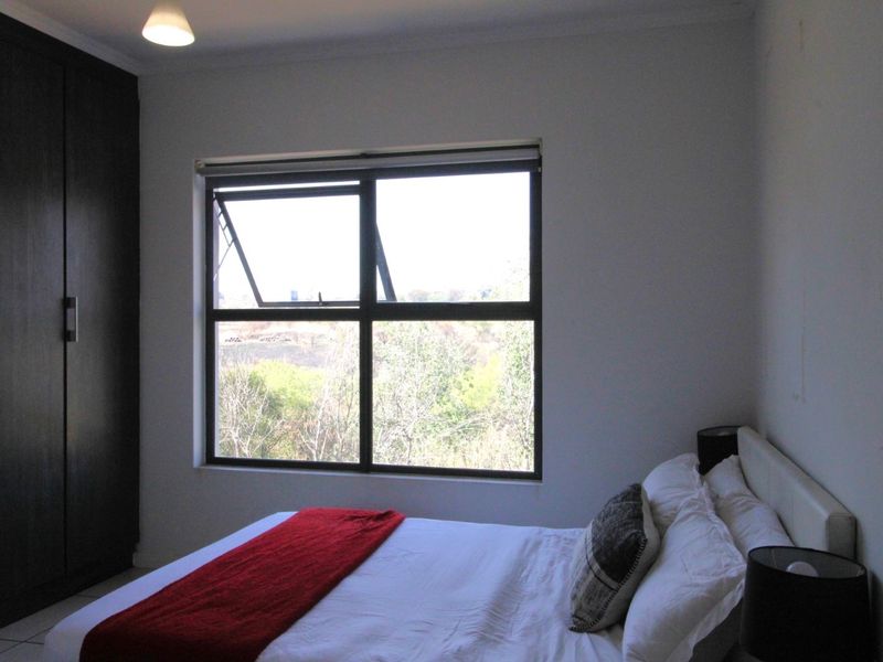 A well-lit bedroom featuring a built-in wardrobe and a large window with views of the surrounding greenery.