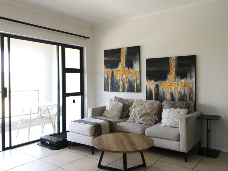 A bright living room featuring tiled flooring and a large sliding glass door providing access to an outdoor balcony area.