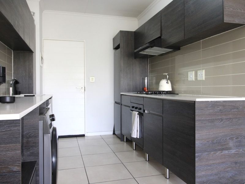 Modern kitchen featuring dark wood-grain cabinetry, stone countertops, integrated gas hob, oven, extractor fan, and neutral tiled flooring.