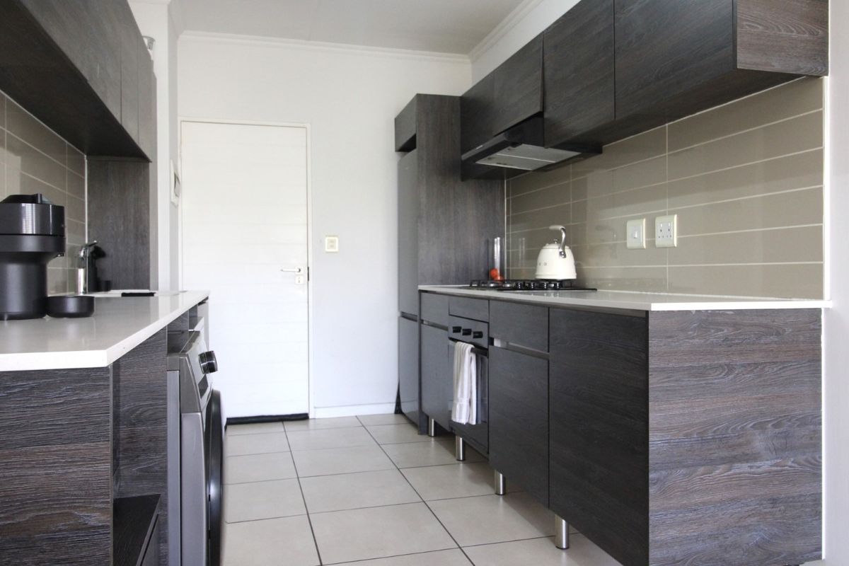 Modern kitchen featuring dark wood-grain cabinetry, stone countertops, integrated gas hob, oven, extractor fan, and neutral tiled flooring.