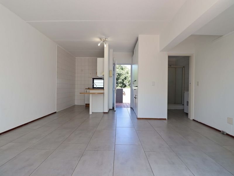 An open-plan living area featuring neutral tiled flooring, leading to a compact kitchen space and a separate bathroom area.
