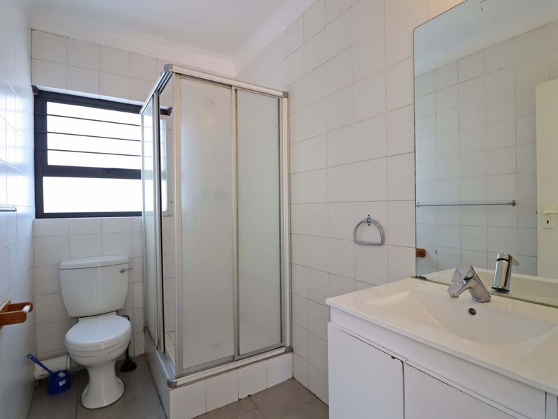 A functional bathroom featuring a shower enclosure, white vanity with basin, wall-mounted mirror, and tiled finishes throughout.
