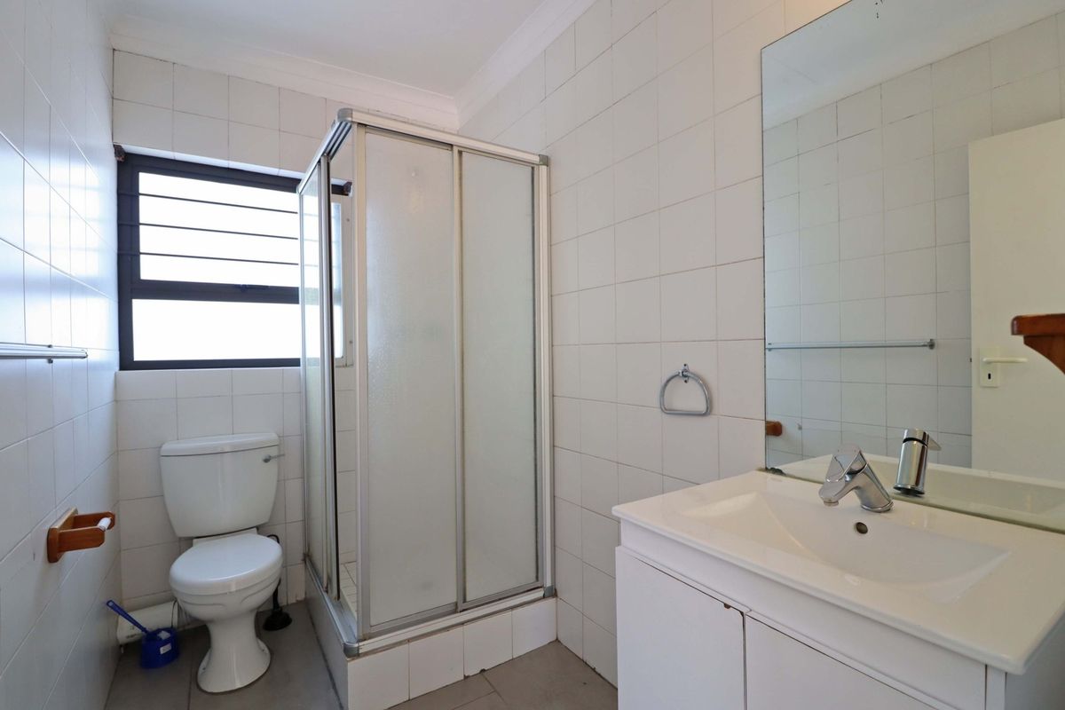 A functional bathroom featuring a shower enclosure, white vanity with basin, wall-mounted mirror, and tiled finishes throughout.
