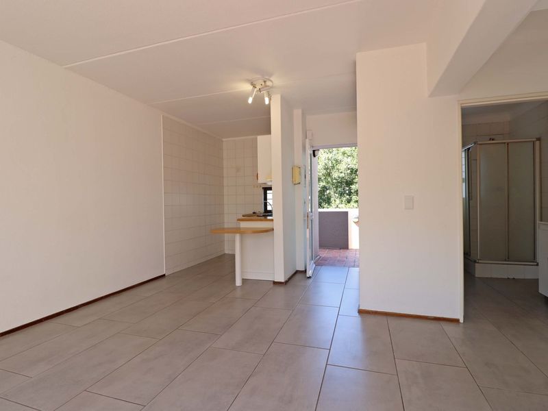 An open-plan living area featuring tiled flooring, a compact kitchen with a breakfast counter, and direct access to an outdoor balcony.
