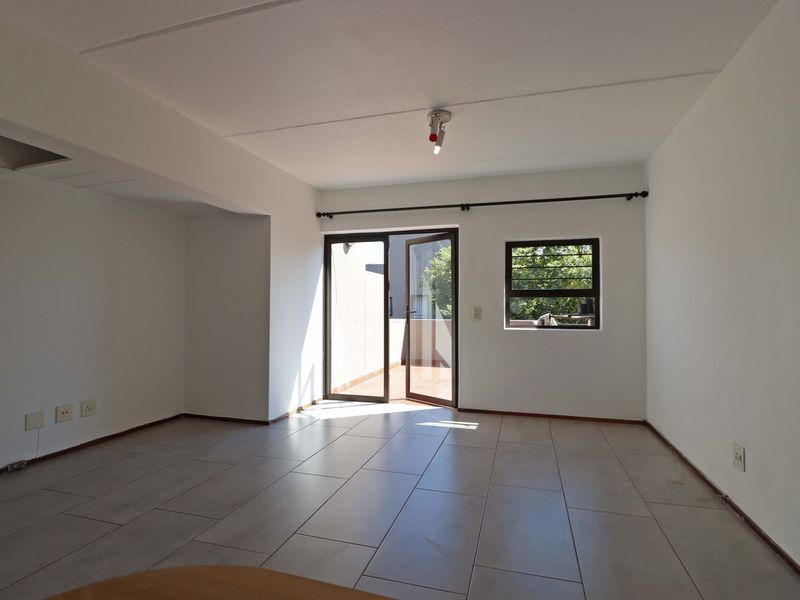 An empty, open-plan living area featuring neutral tiled flooring, natural light, and direct access to an outdoor balcony through a glass door.