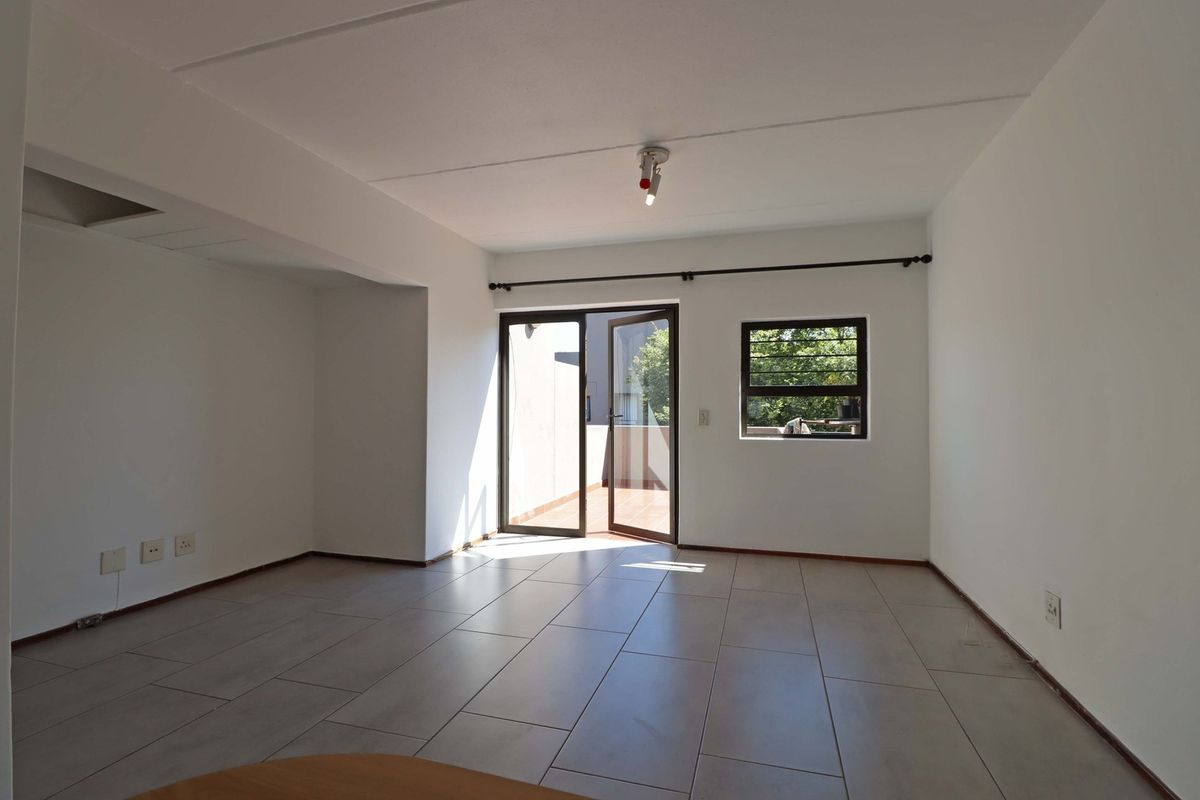 An empty, open-plan living area featuring neutral tiled flooring, natural light, and direct access to an outdoor balcony through a glass door.