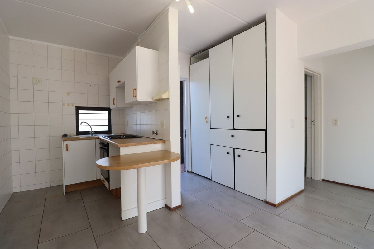 A functional kitchen featuring white built-in cabinetry, tiled splashbacks, a built-in oven and hob, and ample storage space with large pantry cupboards.