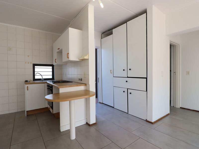 A functional kitchen featuring white built-in cabinetry, tiled splashbacks, a built-in oven and hob, and ample storage space with large pantry cupboards.