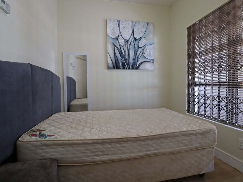A bedroom featuring neutral walls, a window with venetian blinds, and a security gate.