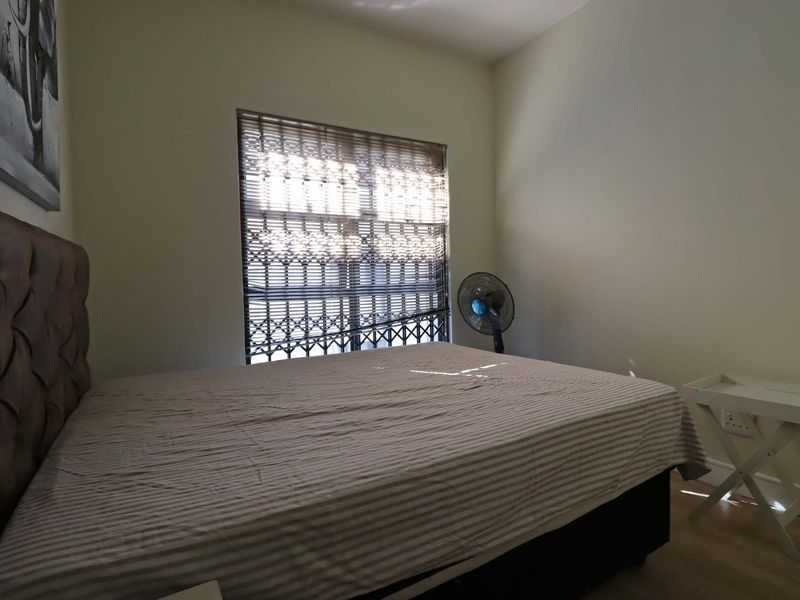 A bedroom featuring laminate flooring and a window fitted with a security gate.
