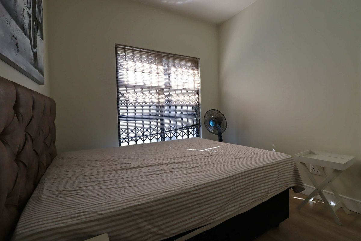 A bedroom featuring laminate flooring and a window fitted with a security gate.