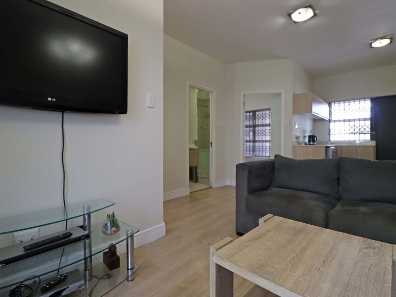Open-plan living area featuring light laminate flooring, recessed lighting, and an integrated kitchen space with security bars on the windows.