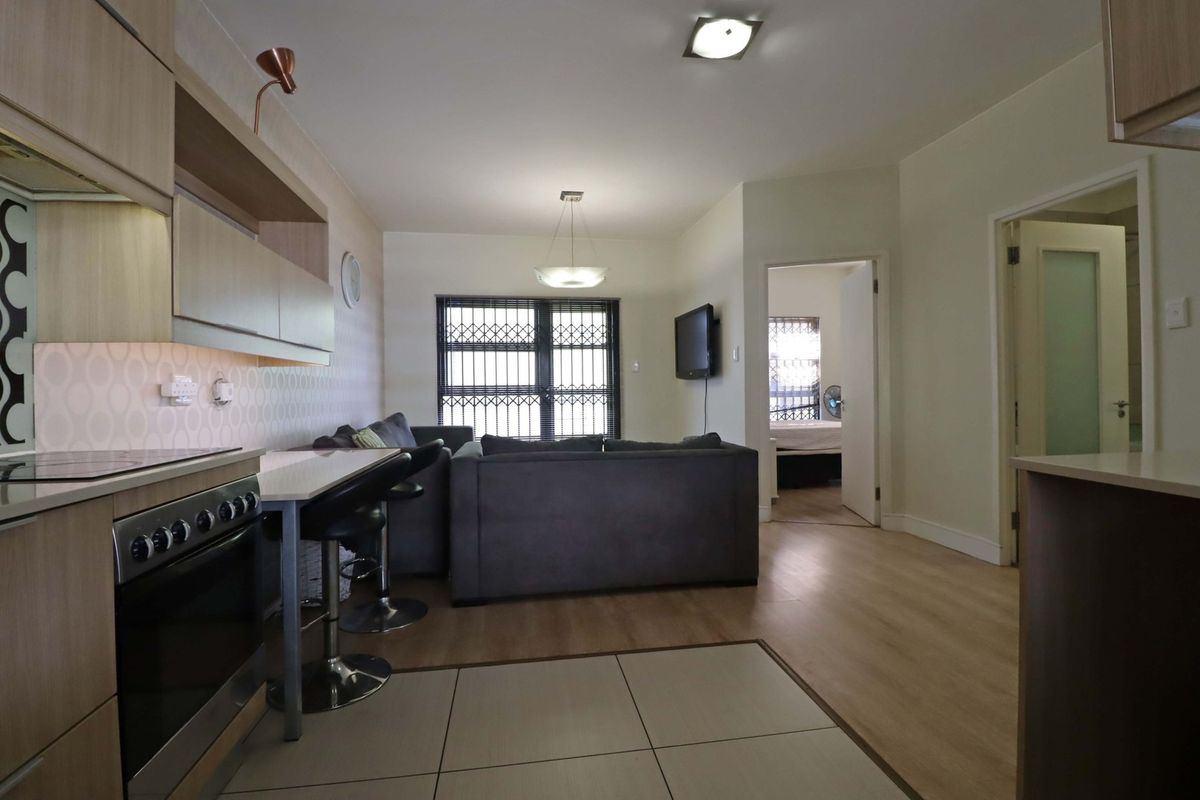 Open-plan living area featuring a modern kitchen with built-in cabinetry, electric stove, and laminate flooring, seamlessly flowing into the lounge space.