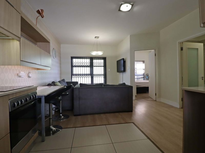 Open-plan living area featuring a modern kitchen with built-in cabinetry, electric stove, and laminate flooring, seamlessly flowing into the lounge space.