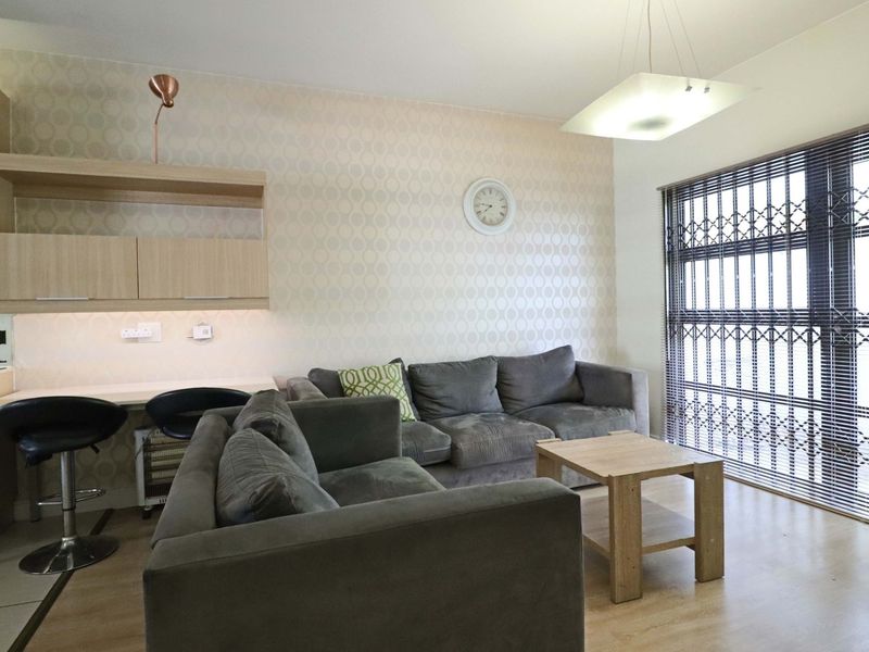 Open-plan living area featuring laminate flooring, built-in kitchen cabinetry, and a large window with a security gate.