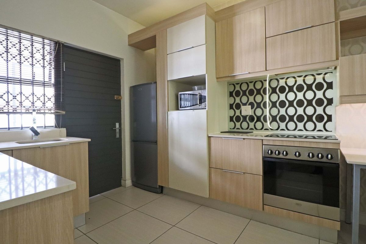 Modern kitchen featuring light wood cabinetry, stone countertops, built-in oven, hob, and a decorative patterned backsplash, offering a clean and functional cooking space.
