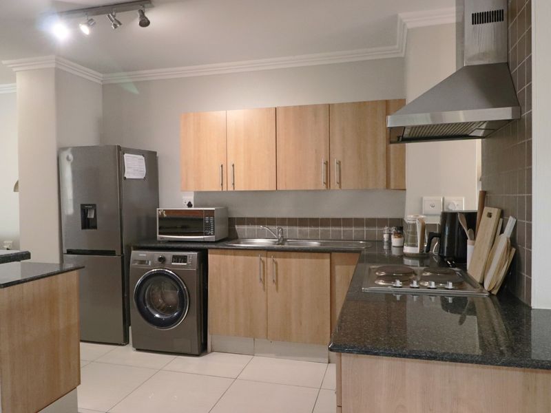 A functional kitchen featuring light wood cabinetry, granite countertops, a stainless steel extractor fan, and integrated space for laundry appliances.