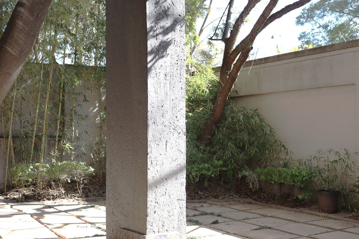 A rear outdoor patio area featuring a concrete support pillar, paved flooring, and a surrounding boundary wall with established garden greenery.