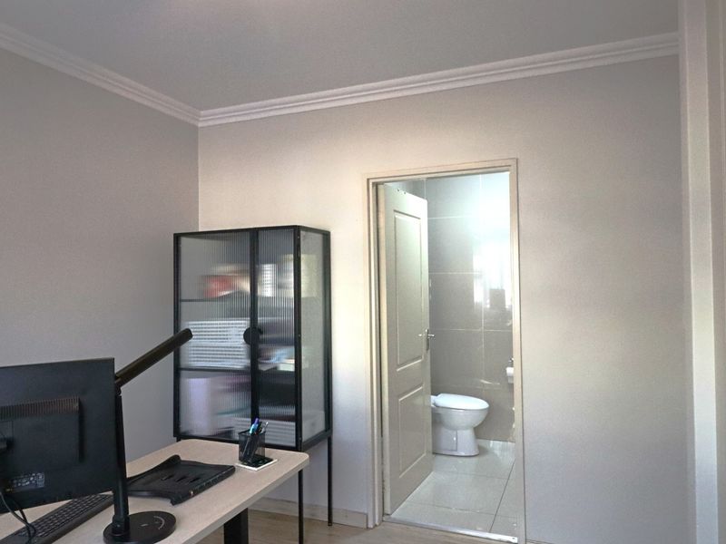 A functional office space featuring neutral walls, coving, and direct access to an adjacent tiled bathroom.