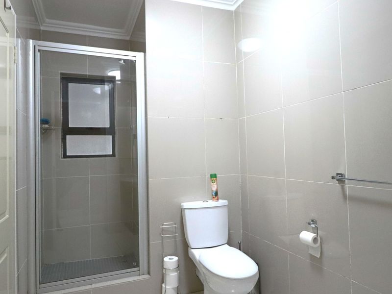A clean, modern bathroom featuring a glass-enclosed shower, neutral wall tiling, and standard sanitary fixtures.
