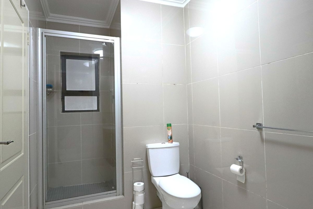 A clean, modern bathroom featuring a glass-enclosed shower, neutral wall tiling, and standard sanitary fixtures.