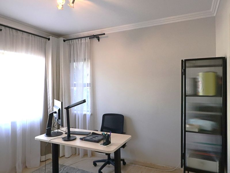 A bright home office space featuring neutral walls, crown molding, and large windows with installed curtain rods.