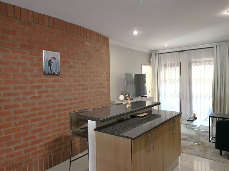 Open plan living area featuring an exposed brick wall, granite breakfast bar, tiled flooring, and sliding doors leading to an outdoor space.